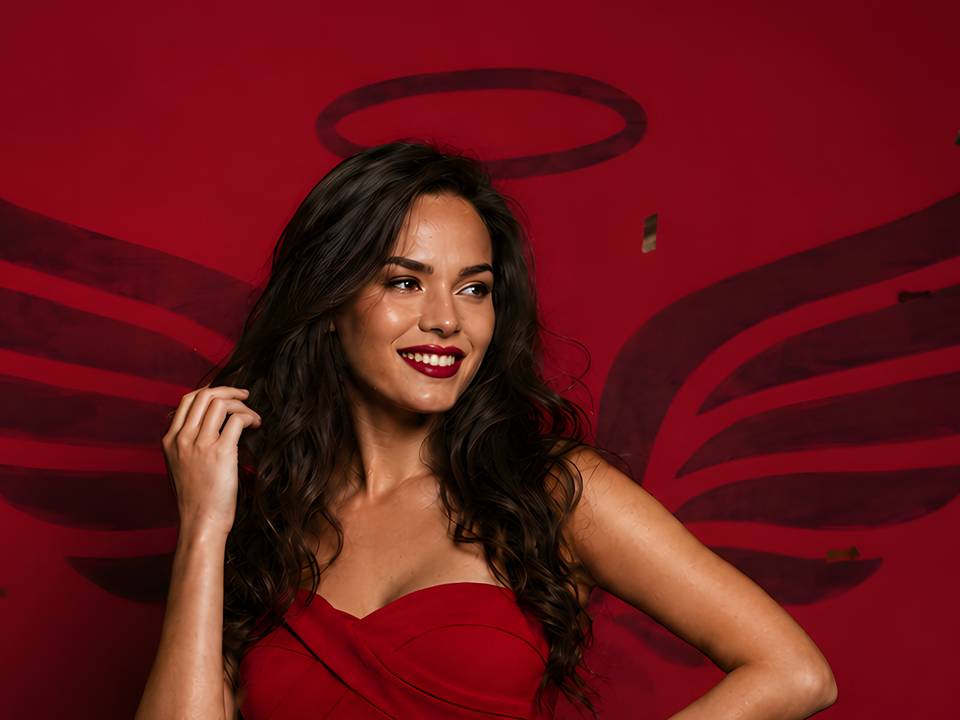 Vizual de prezentare Red Angels: un model în rochie roșie, în fața logo-ului cu aripi și aureolă
