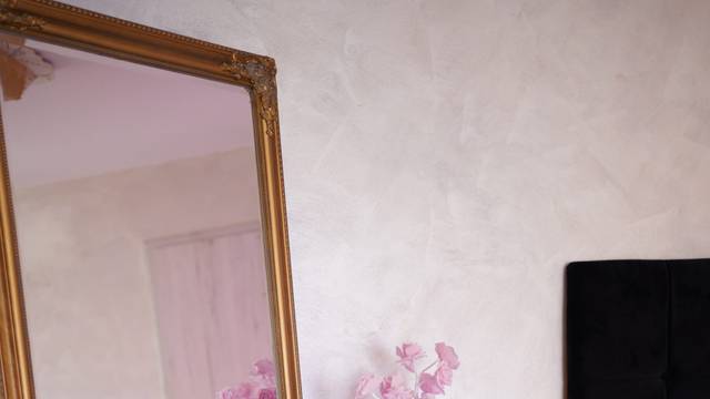Detaliu din studioul Red Angels: oglindă cu ramă aurie pe toată înălțimea, măsuță rotundă aurie și decor floral roz
